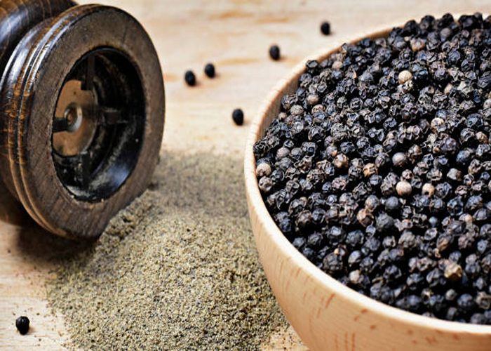 Black peppercorns and milled pepper, arrangement in a wooden bowl. Close up shot of black pepper, cooking ingredient scene and wooden table. Top view.